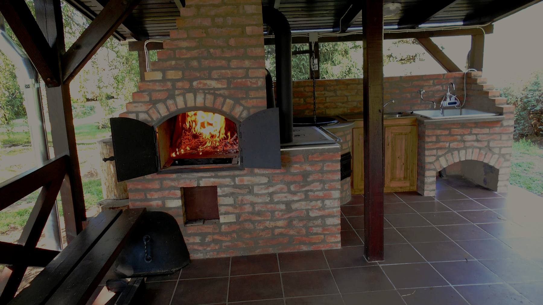 Lángoló tűz a téglakemencében a fedett pavilon alatt, sötét esti tónusban.