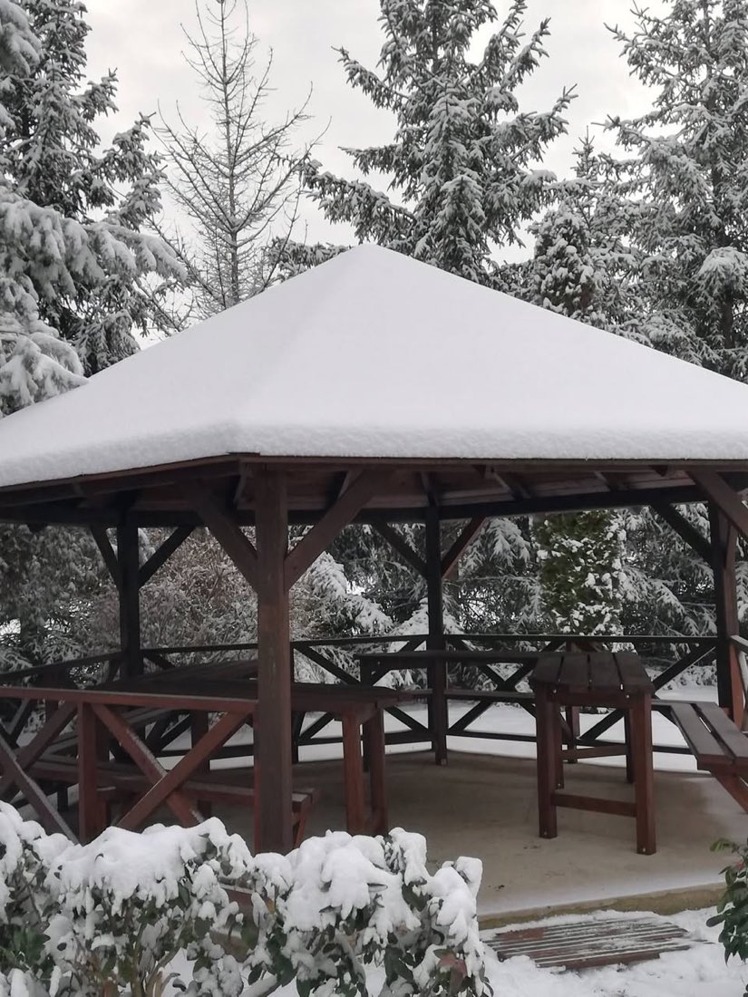 A kerti pavilon vastag hótakaró alatt, körülötte havas fenyők.